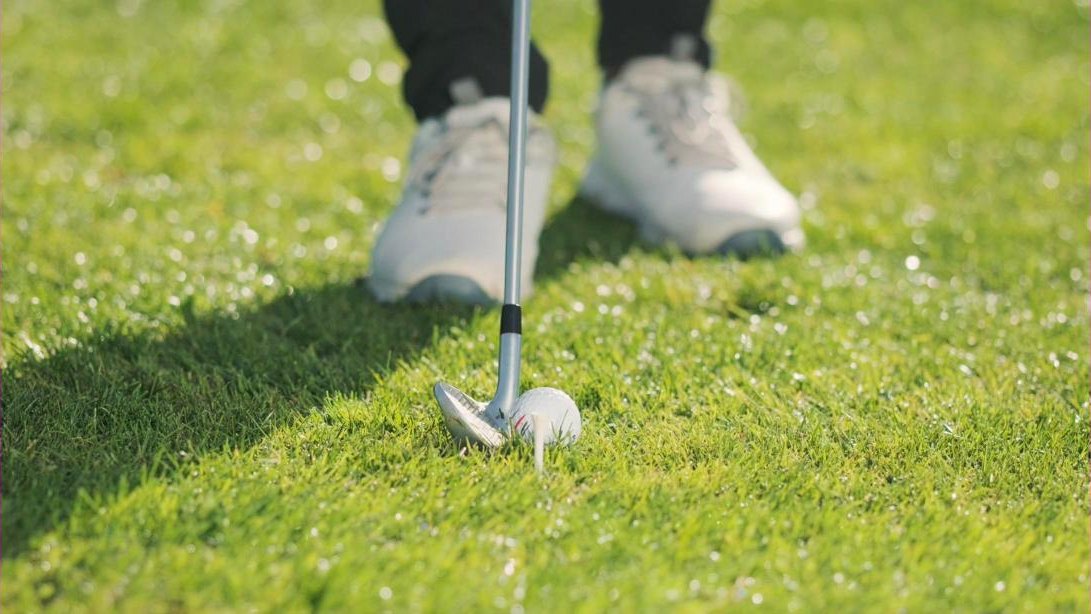 Face d'un fer de golf posée juste derrière la balle dans l'herbe rase