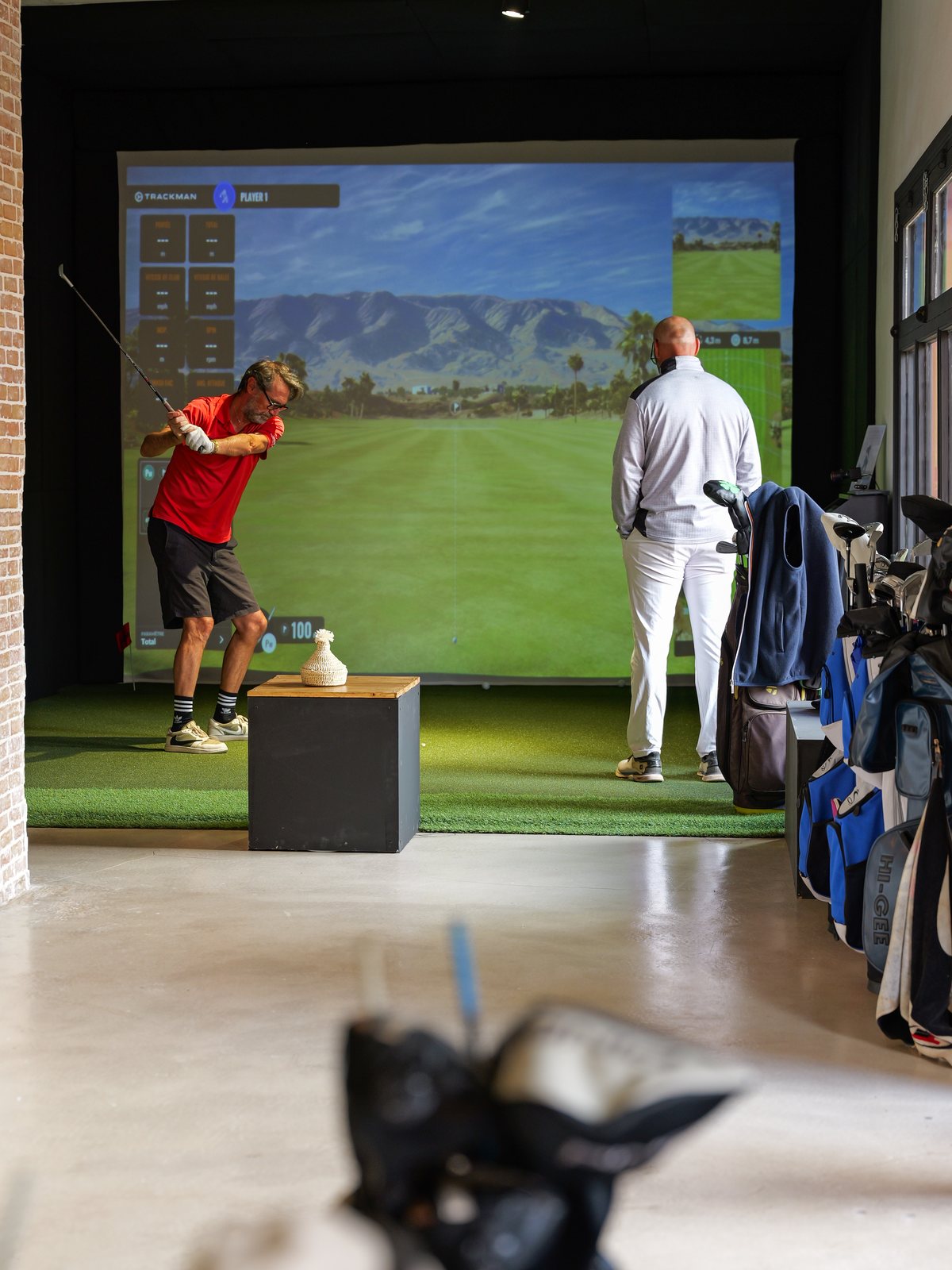 Joueur au swing sur une baie du G.Spot, sacs de golf alignés